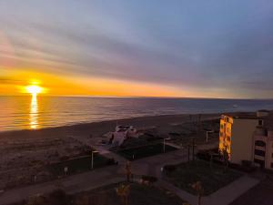 - un coucher de soleil sur la plage avec un bâtiment et l'océan dans l'établissement Appartement de vacances - Splendide vue sur mer, Parking privé, au Barcarès