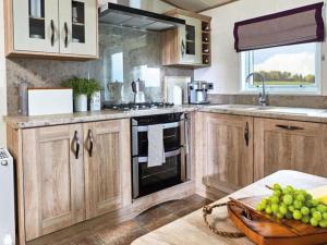 a kitchen with wooden cabinets and a bowl of grapes at Unwind@13 Badger Lakes, Haggerston, Northumberland in Beal