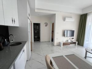 a white kitchen with a sink and a living room at Art life apart (Meadow) in Alanya