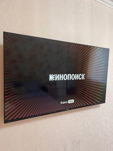 une télévision sur un mur portant le nom d'une société dans l'établissement Уютная в центре на Дом быта /Smart TV, à Uralsk