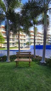 a wooden bench in a park with palm trees at Apartamento Confortável - Porto das Dunas - Perto do Beach Park in Aquiraz