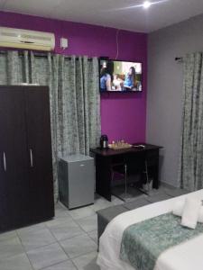 a bedroom with a bed and a tv on the wall at De Ellas Boutique Lodge in Polokwane
