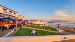 a group of people sitting on the grass near the ocean at The Blue Peter Hotel in Cape Town