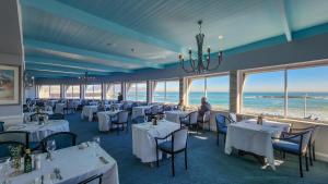 a dining room with white tables and chairs and the ocean at The Blue Peter Hotel in Cape Town