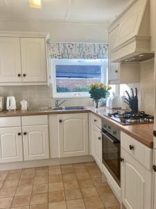cocina con armarios blancos, fregadero y ventana en Mariners Corner en Bexhill
