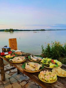 a wooden table with plates of food on it next to a lake at The Secret Garden Camping - Hồ Trị An 