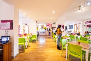 a woman standing in a dining room with green chairs at Safestay Pisa Centrale in Pisa