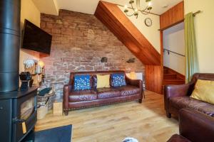 een woonkamer met leren banken en een stenen muur bij 2 Eden Grove Cottages in Armathwaite