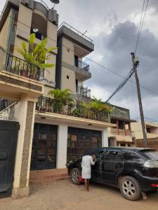 a woman standing next to a black car in front of a building at Nelly Apartments in Mbale