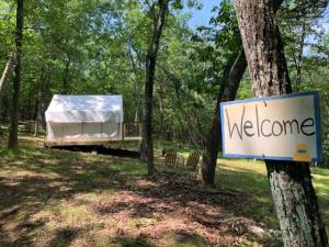 a sign that says welcome with a camper in the woods at Sweet Hill Glamping in Rhinebeck