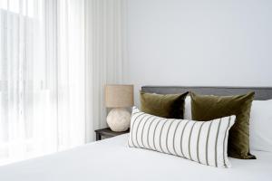 Una cama blanca con almohadas y una lámpara en una mesa. en Birch Apartments by the Lake, en Canberra