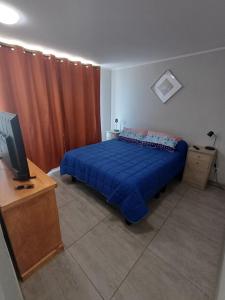 um quarto com uma cama azul e uma televisão em Departamento Ines de Suarez, La Florida em Santiago