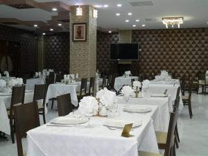 una sala da pranzo con tavoli e sedie bianchi e una TV di Hôtel Lina a Bordj Bou Arreridj