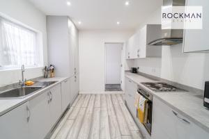 a kitchen with white cabinets and a wooden floor at Spacious 7 Bed House with Garden by Rockman Stays in Southend-on-Sea