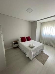 um quarto branco com uma cama com 2 almofadas vermelhas em Sobrado com piscina, banheira e garagem coberta. em Piçarras