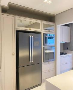 uma cozinha com um frigorífico de aço inoxidável e armários brancos em Sobrado com piscina, banheira e garagem coberta. em Piçarras