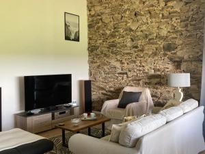 a living room with a couch and a tv and a stone wall at « La Crécerelle » spacieux gîte contemporain entre Tarn et Aveyron in Sainte-Gemme