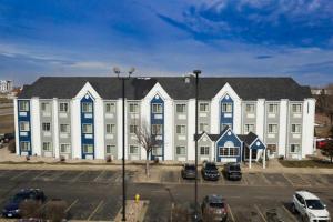 Microtel Inn & Suites by Wyndham Sioux Falls في شلالات سيوكس: مبنى ابيض كبير بنوافذ زرقاء وموقف سيارات