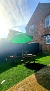 a picnic table with a green umbrella on the grass at Watford Gem Private Garden Mins to Harry Potter Studio in Watford