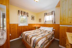 a bedroom with a bed with wooden walls and a window at Fiddler's Green Country Cottages in Brackley Beach