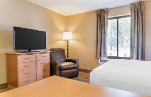 ein Hotelzimmer mit einem Bett, einem TV und einem Stuhl in der Unterkunft Extended Stay America Select Suites - Detroit - Warren in Warren