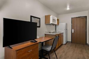 a small kitchen with a desk with a large flat screen tv at WoodSpring Suites Champaign near University in Champaign