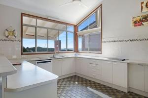 una cocina con armarios blancos y una ventana en Siesta by the Sea, en Coffs Harbour