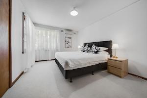a white bedroom with a large bed and a night stand at Spacious 4-bed Family Home in Tranquil Setting in Canberra