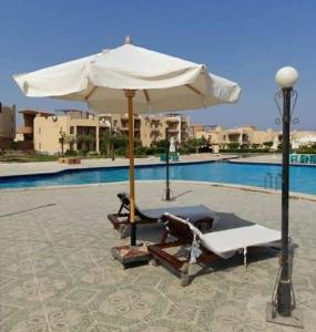 a white umbrella and lounge chairs next to a pool at Studio with pool view at Bella Vista resort sokhna in Ain Sokhna