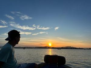 Un uomo seduto su una barca che guarda il tramonto di Song Suoi Quy Nhon Beachfront Apartment a Quy Nhon