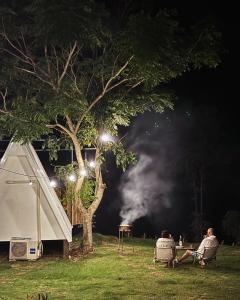 two people sitting in chairs under a tree at night at Tid Khao Glamping & Bar in Tha Kradan