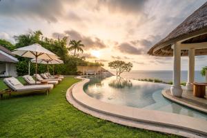 a resort pool with lounge chairs and the ocean at Villa Nirvana Biru Bingin Beach in Uluwatu