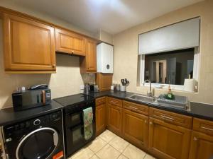 a kitchen with wooden cabinets and a black dishwasher at Spacious 4BR Home Near The NEC The Airport and Heartlands Hospital in Birmingham