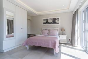 una camera bianca con un letto con una coperta rosa di Your Cozy Haven in Chanteclaire a Hermanus