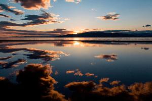 una puesta de sol sobre el agua con nubes en el cielo en Kampaoh Delta del Ebro, en El Poblenou del Delta