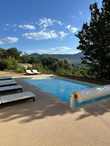 a swimming pool with two loungers and two loungers next to at Le Mas des Eglantiers in Propiac