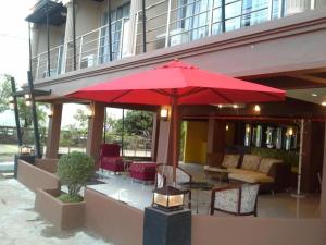 Baan Rim Khong Hotel في Ban Nong Saeng: فناء فيه مظلة حمراء وطاولات وكراسي