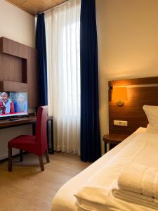 - une chambre avec un lit, une chaise rouge et une télévision dans l'établissement Hotel Fränkischer Hof, à Kitzingen