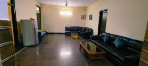 ein Wohnzimmer mit schwarzen Ledersofas und einem Kühlschrank in der Unterkunft VB dormitory in Neu-Delhi