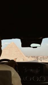 Pyra Hospitality West Pyramids Cairo في القاهرة: شخص يقود سيارة امام الاهرامات