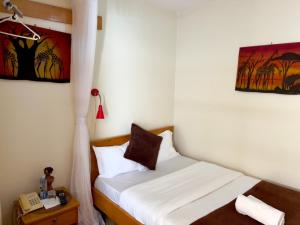 um pequeno quarto com uma cama com lençóis brancos em Sunset Hotel Entebbe em Entebbe