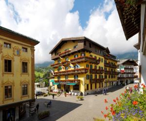 een geel gebouw in een stad met mensen die er omheen lopen bij Hotel De La Poste in Cortina dʼAmpezzo