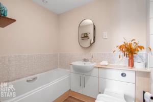 een badkamer met een bad, een wastafel en een spiegel bij OnSiteStays 2BR, Parking, Wifi, Shops and Restaurants Close in Hatfield