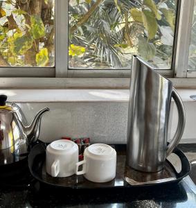 a tea kettle and two cups on a counter next to a window at Easy Living Guesthouse in Orlim