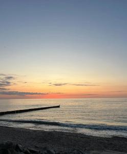 plaży z molo i oceanem o zachodzie słońca w obiekcie Wakacyjna Wioska w mieście Ustronie Morskie