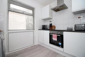 a kitchen with white cabinets and a window and a stove at Peaceful 3 Bed Flat with Parking and Balcony by CTO Serviced Apartments in Cardiff