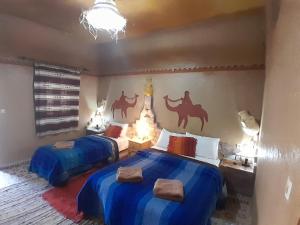 um quarto com 2 camas com lençóis azuis e pinturas de camelo na parede em Auberge Camping La Liberté em Merzouga