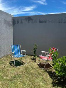 twee stoelen in het gras naast een muur bij Apto 104: sol, mar e conforto. in Rio das Ostras