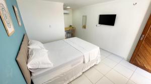a bedroom with a white bed and a television at Pousada Maré Forte in Cascavel