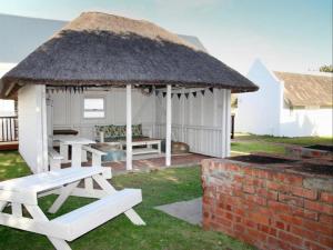 a gazebo with two picnic tables and a thatch roof at Seals Backpackers in Cape St Francis